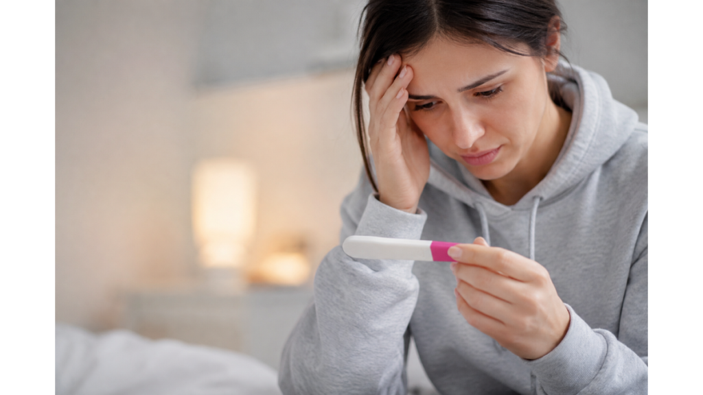 Woman looking at a positive pregnancy test while experiencing early chemical pregnancy symptoms before bleeding, representing a biochemical pregnancy.